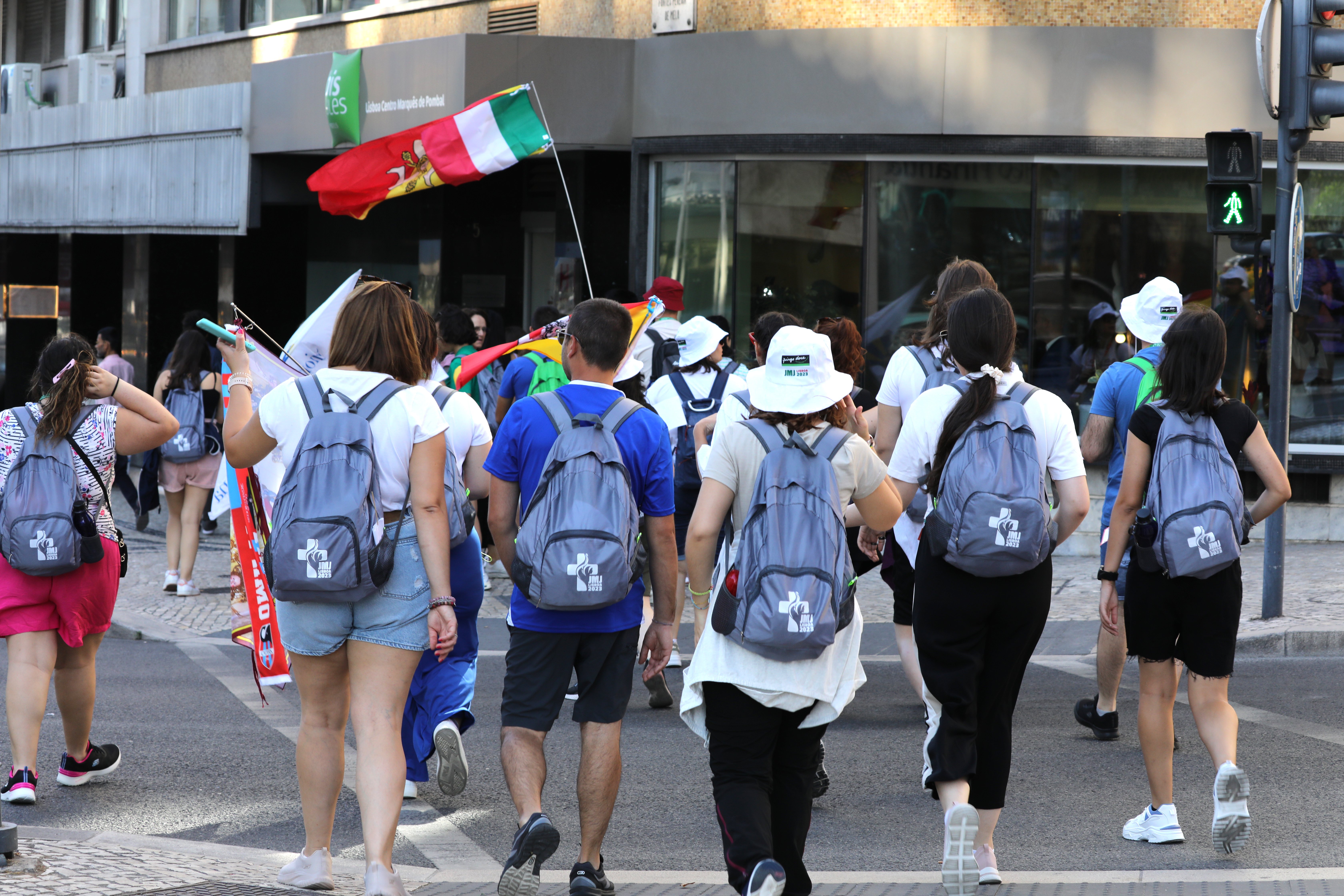 a line of about seven pilgrims walk the streets of Lisbon in matching backpacks and following a flag of Portugal